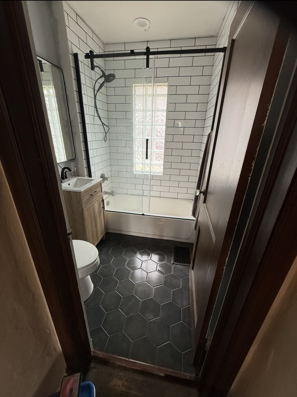 Bathroom after — white subway tile surround, matte black fixtures, sliding glass door, and hex tile floor