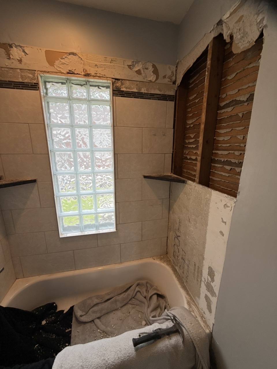 Bathroom before — dated tile, glass block window, and walls opened to studs and lath
